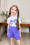 Kız Çocuk Üzerinde Digital Kurdela Basklı T-Shirt ve Fiyonk Cep Detaylı Lila Şortlu Takım